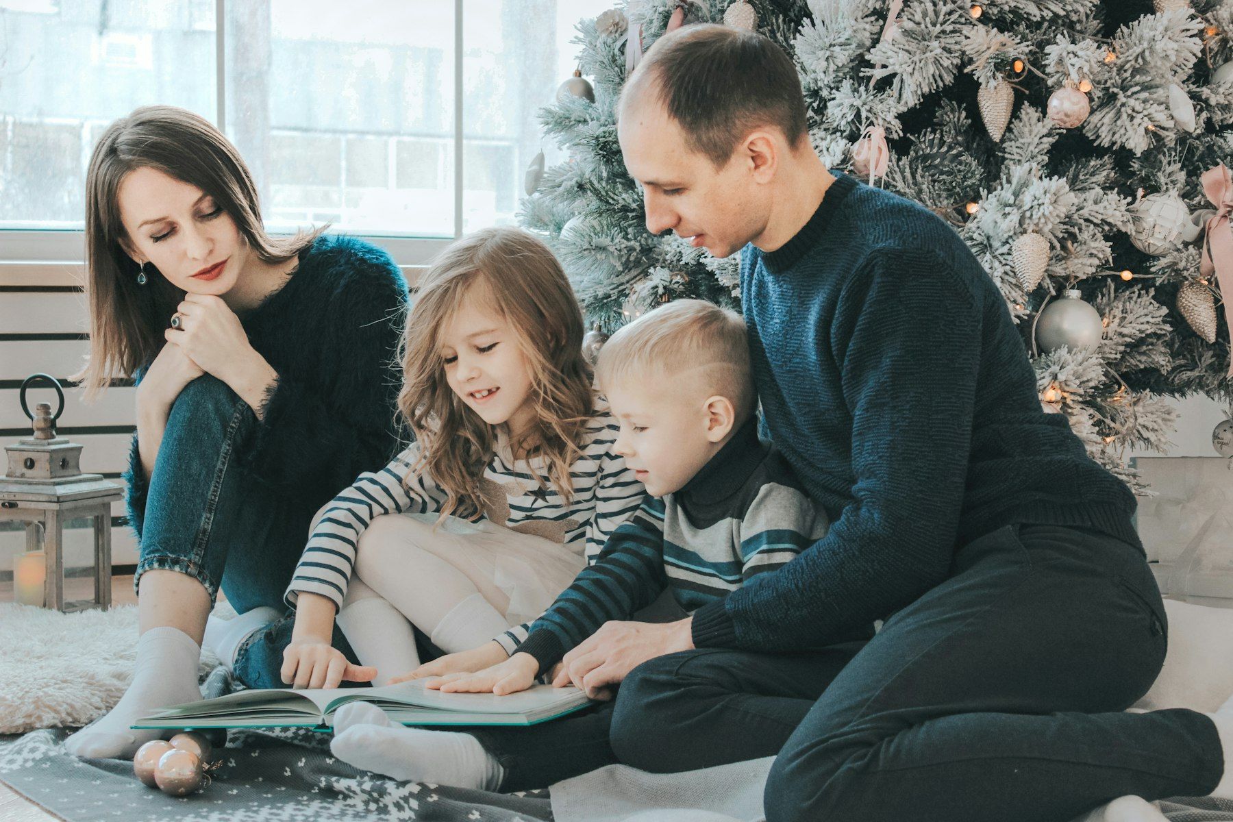 Des parents lisent une histoire à leurs enfants près du sapin